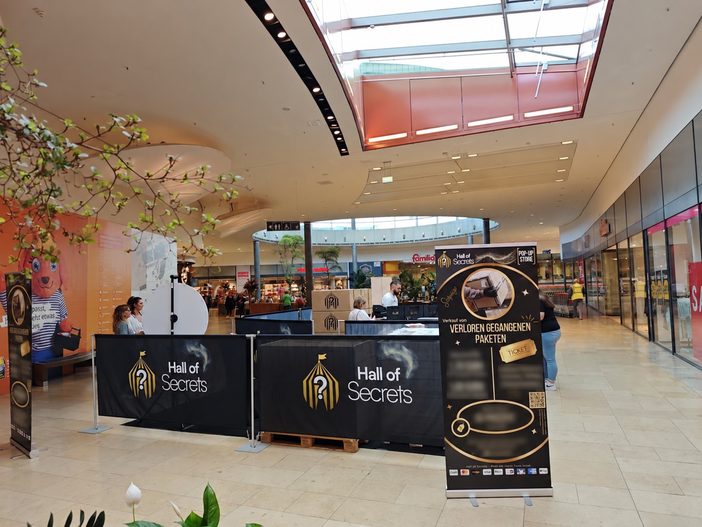 Der Hall-of-Secrets-Stand im Einkaufscenter mit schwarz-goldenen Bannern und großen Hall-of-Secrets-Logos.